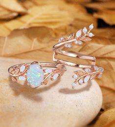 an opal and diamond ring sitting on top of a leaf - shaped rock with leaves surrounding it