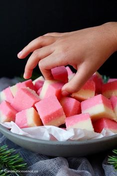 a person reaching for some pink and white squares in a bowl with pine branches on the side