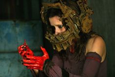 a woman with red paint on her face and hands holding a piece of metal equipment