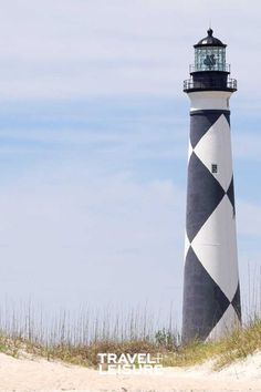 a black and white lighthouse sitting on top of a sandy beach next to tall grass