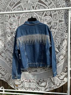 Add sparkle to any outfit with this denim jacket with rhinestone fringe along the back. Perfect for the rodeo, concert or to pair with any outfit.  Wash instructions: spot clean or hand wash only. Drip dry only Materials: Faux rhinestone set in place using monofilament illusion cord with at least one stitch in between every rhinestone. Festival Denim Fringe Outerwear, Spring Denim Jacket With Beaded Fringe And Long Sleeves, Fall Denim Jacket With Beaded Fringe And Long Sleeves, Long Sleeve Denim Jacket With Rhinestone Fringe, Trendy Denim Jacket With Rhinestone Fringe For Fall, Trendy Spring Denim Jacket With Rhinestone Fringe, Casual Denim Jacket With Rhinestone Fringe, Casual Long Sleeve Denim Jacket With Rhinestone Fringe, Fall Denim Outerwear With Rhinestone Fringe