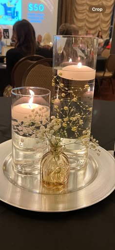 two vases filled with water and flowers on top of a silver plate at a table