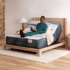 a man reading a book while sitting on a bed with a wooden frame and mattress