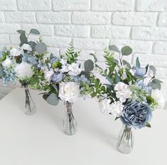 three vases filled with flowers on top of a white table next to a brick wall