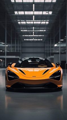 an orange sports car is parked in a large garage with its doors open and lights on