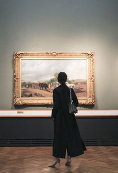 a woman standing in an art gallery looking at a painting on the wall behind her