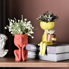 two vases with flowers are sitting on top of books and one has a face