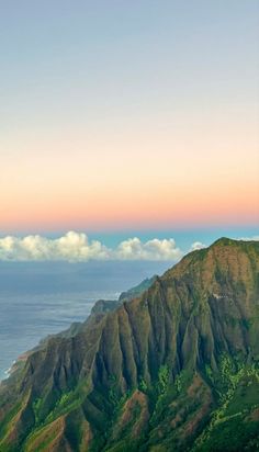 the top of a mountain with some clouds in the sky above it and water below