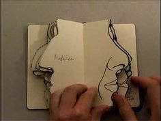 a hand holding an open notebook with drawings on it and writing in the pages that have been drawn