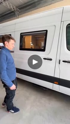 a man standing next to a white van in a garage with an open door and windows