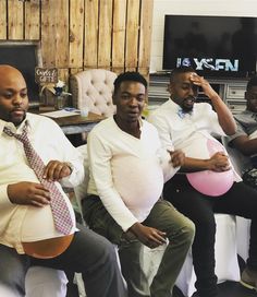 three men sitting in chairs with one holding a pink ball while the other holds a pink balloon