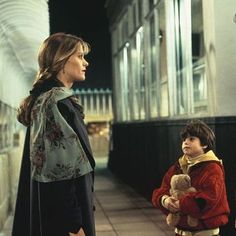 two women and a young boy standing on a sidewalk at night, one holding a teddy bear