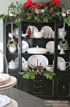 a black china cabinet decorated for christmas with greenery and poinsettis