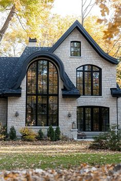 a white brick house with black windows and lots of fall leaves on the ground in front of it