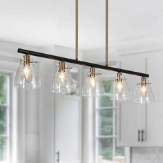 a kitchen light fixture with five clear glass shades hanging from it's brass finish