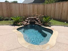 a small swimming pool in the middle of a backyard with rocks and plants around it