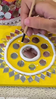 a person is using a paint brush to decorate a yellow and white object with mirrors