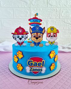 a birthday cake with three dogs on top and paw patrol decorations in the middle, sitting on a pink tablecloth