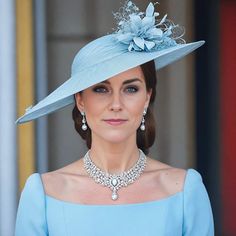 a woman in a blue dress and hat with jewels on her neck is looking at the camera