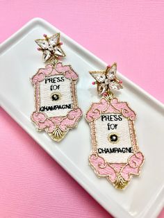 two pink and gold earrings on a white plate with the words press it for champagne