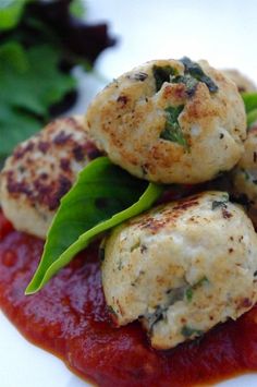 some meatballs are sitting on top of tomato sauce and green leafy garnish