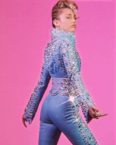 a woman in blue jumpsuit walking on pink background