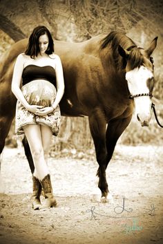 a pregnant woman standing next to a horse