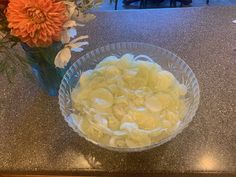 a glass bowl filled with sliced bananas on top of a counter next to a vase full of flowers