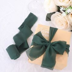 a gift wrapped in green ribbon next to some flowers and wine glasses on a table