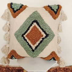 a decorative pillow with tassels on the sides and fringe around the edges, sitting on a shelf