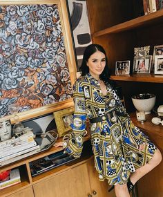 a woman standing in front of a book shelf next to a wall with pictures on it