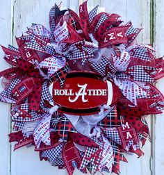 Showcase your Alabama Crimson Tide pride with this eye-catching wreath! Crafted from vibrant crimson and white ribbon mesh, it features the iconic 'Roll Tide' logo front and center. Adorned with polka dots, houndstooth patterns, and Bama themed ribbons, this wreath exudes Southern charm. Hang it on your front door to welcome guests in true Alabama style or display it indoors as festive decor for game days. With its intricate design and team spirit, this wreath is a must-have for any devoted Crimson Tide fan. Dimensions: 24 inches in diameter. Alabama Front Door Sign, Round Alabama Door Hanger, Alabama Crimson Tide Christmas Wreath, Alabama Football Wreath, Alabama Door Hanger, Tide Logo, Alabama Decor Crimson Tide, Crimson Tide Fans, Football Wreath