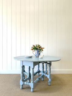 a blue table with flowers on it in front of a white wall and beige carpet