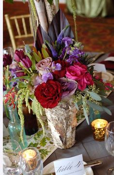 an arrangement of flowers and greenery on a table with place cards for guests to sit at