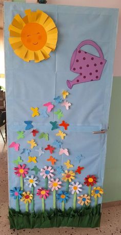 a door decorated with paper flowers and a watering can on the outside, in front of a blue wall