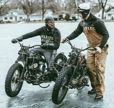 two men standing next to each other on motorbikes in the snow and ice