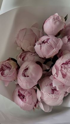 a bouquet of pink peonies in a white paper wrapper on a table