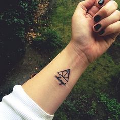 a woman's wrist with a small triangle and arrow tattoo on her left arm