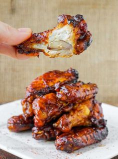 someone is taking a bite out of chicken wings on a white plate with some sauce