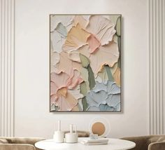 an abstract painting hangs on the wall above a white table with two beige chairs in front of it