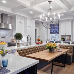 a kitchen with white cabinets and a wooden table in the center surrounded by brown leather benches