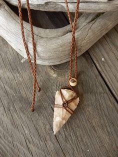 two necklaces on a wooden surface one has a shell and the other has a beaded cord