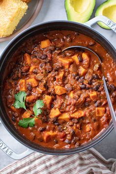 a bowl of chili with bread and avocado on the side next to it