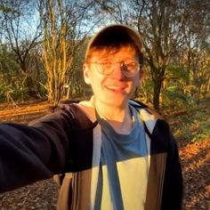 a man taking a selfie in front of some trees and bushes with his hands out