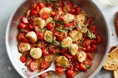 a pan filled with tomatoes and scallops on top of a table next to bread