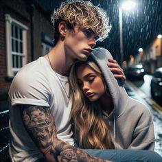 a man and woman sitting next to each other in the rain with their arms around each other