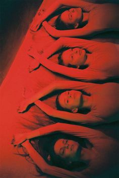 four women are standing in a row with their heads turned to the side, all wearing red dresses