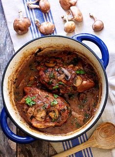 a blue pot filled with meat and mushrooms on top of a table next to garlic