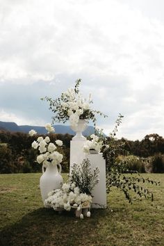 two white vases with flowers and greenery on the grass