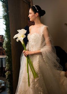 a woman in a wedding dress holding a white flower and wearing a tulle veil